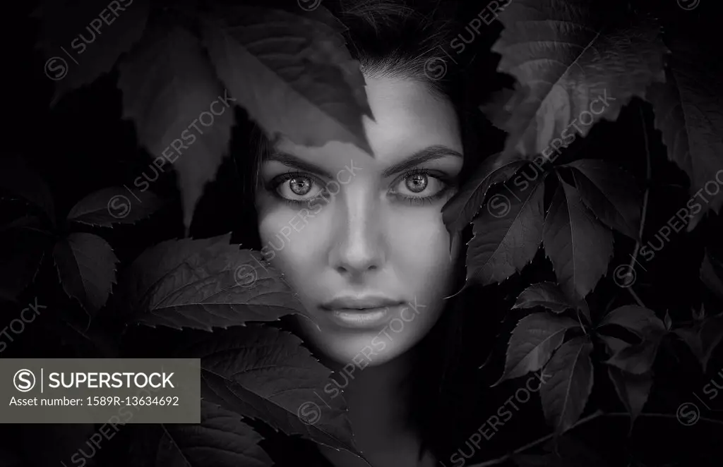Face of Caucasian woman behind foliage