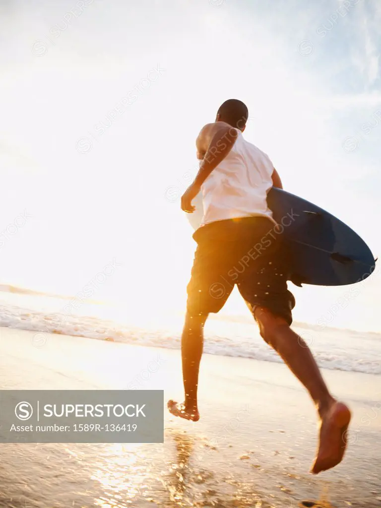Black man running with surfboard on beach
