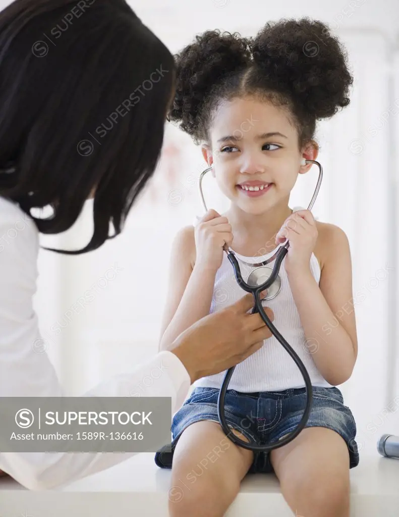 Pediatrician helping patient listen to heartbeat.