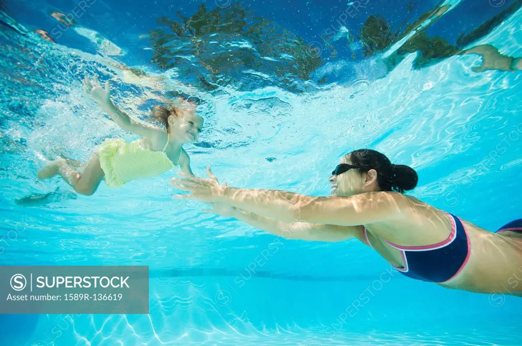 Mother swimming in swimming pool with daughter