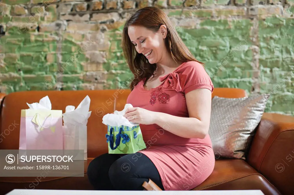 Pregnant Caucasian woman opening baby shower gifts