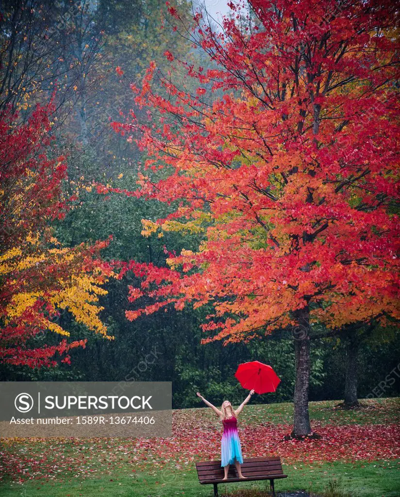 Caucasian woman holding umbrella in rain on park bench
