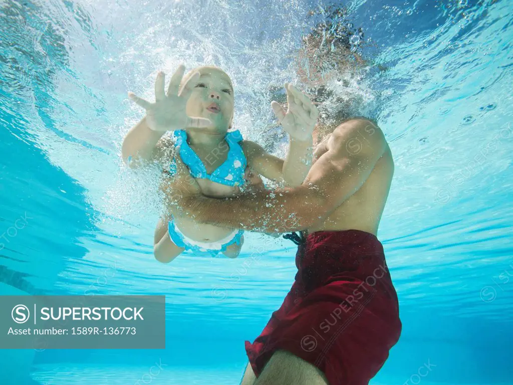 Mixed race father holding daughter in swimming pool