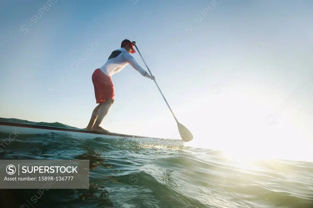 Mixed race man paddling on surfboard