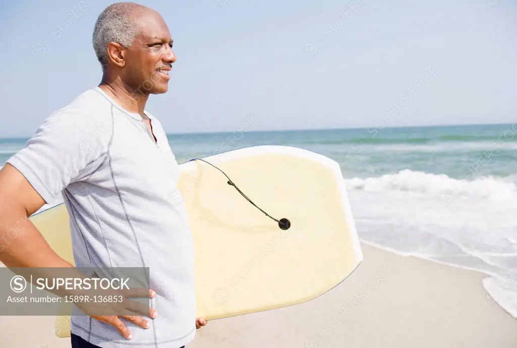 Black man holding body board on beach