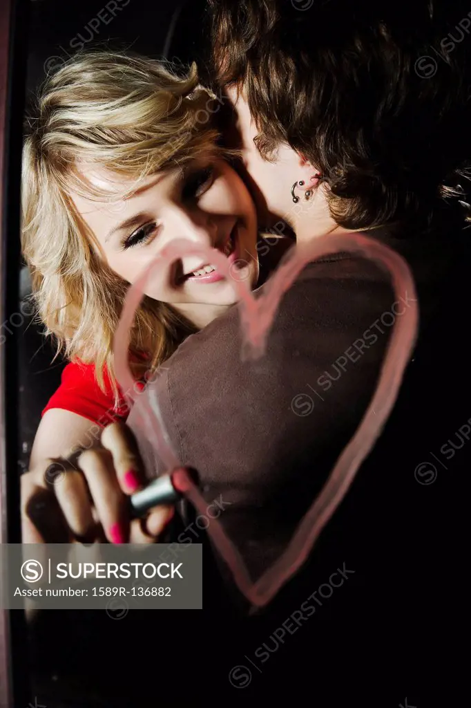 Woman drawing heart with lipstick on mirror while hugging boyfriend