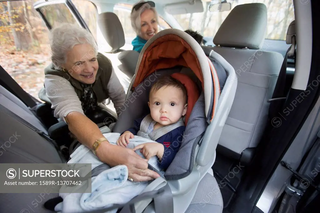 Grandmother fastening baby grandson in car seat