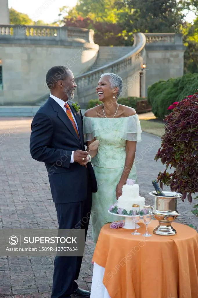Black couple laughing near wedding cake