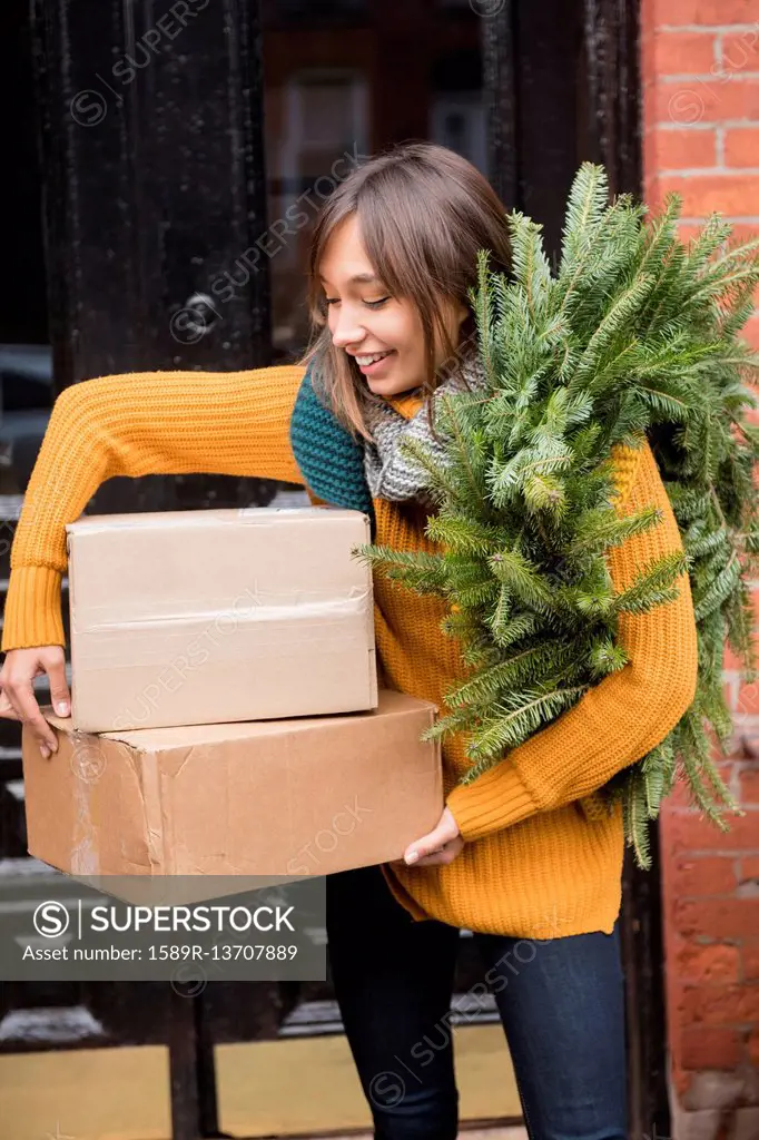 Mixed Race woman carrying pine wreath and cardboard boxes