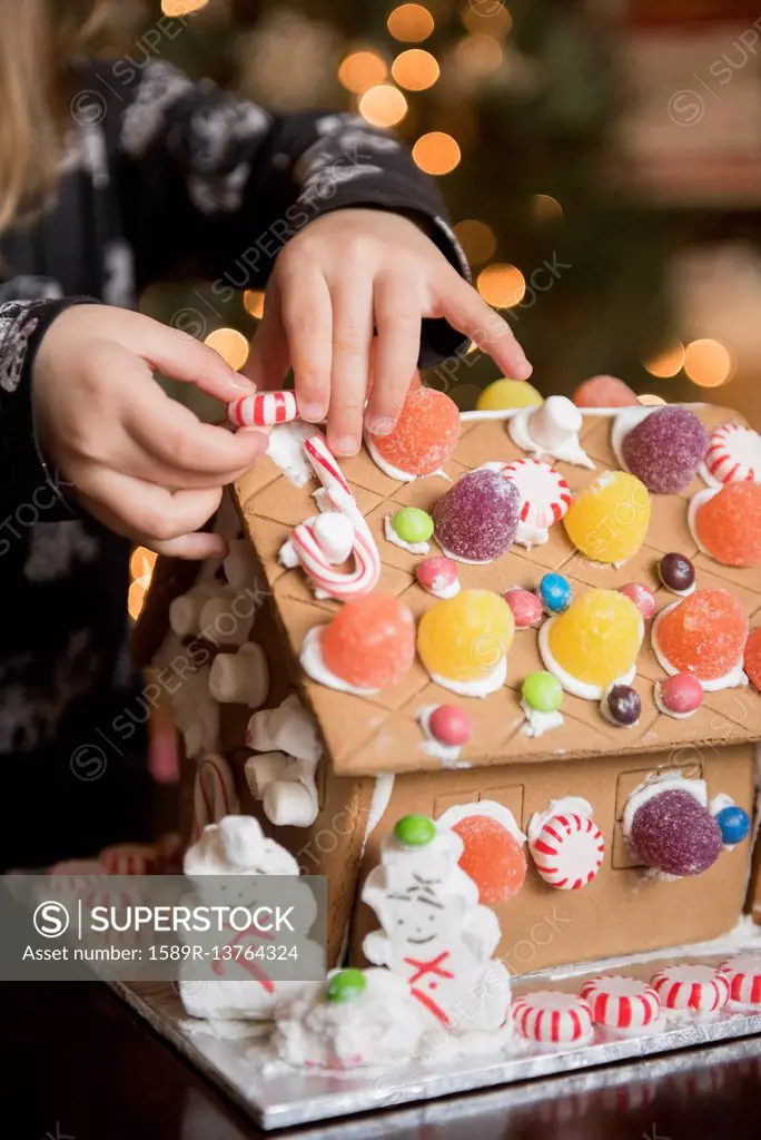 Hands of Caucasian girl decorating gingerbread house with candy