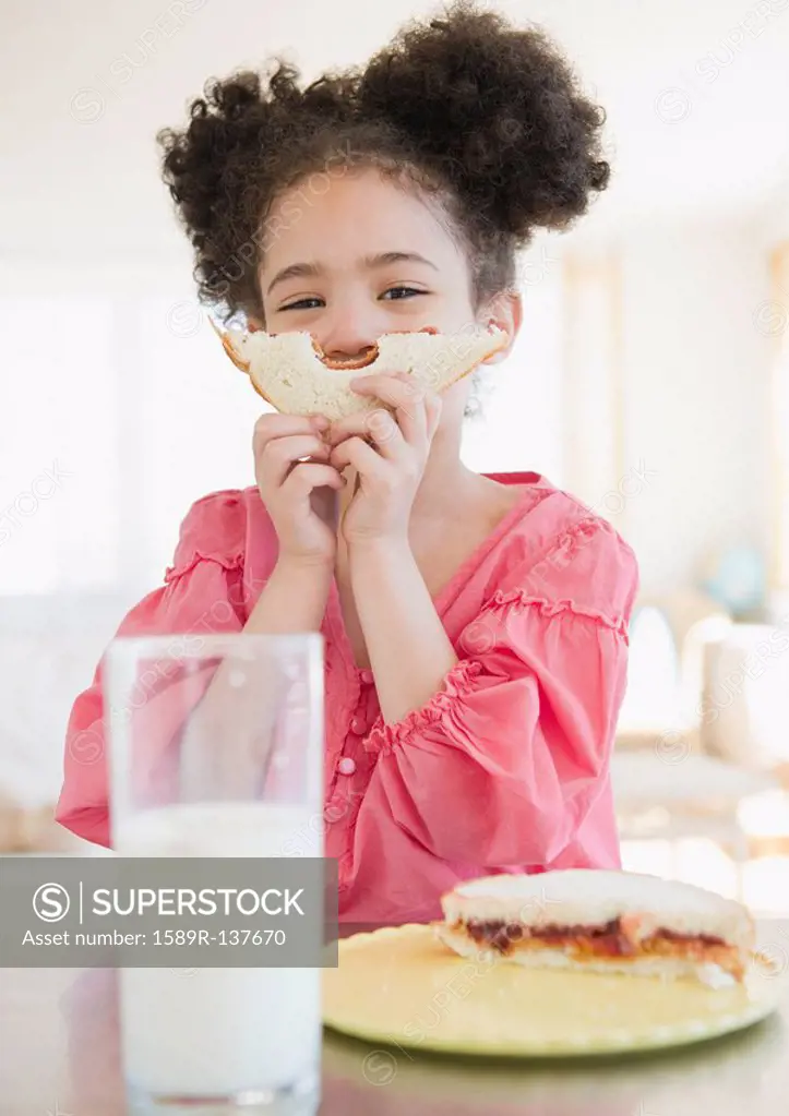 Mixed race girl holding sandwich in front of face