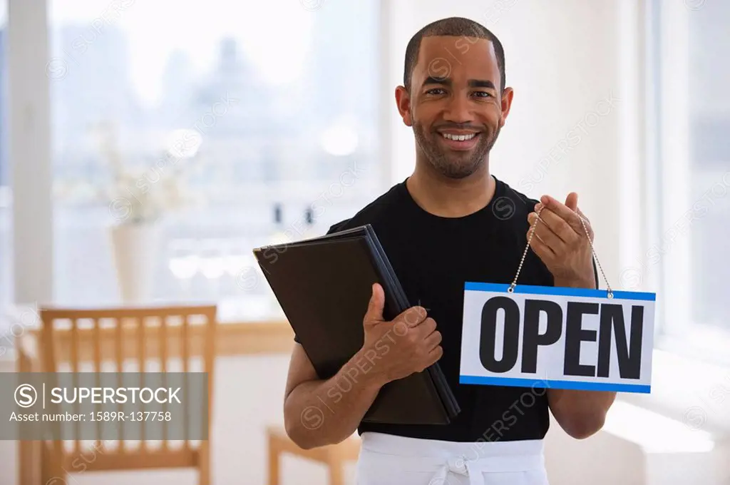 Mixed race waiter in restaurant holding menu and open sign