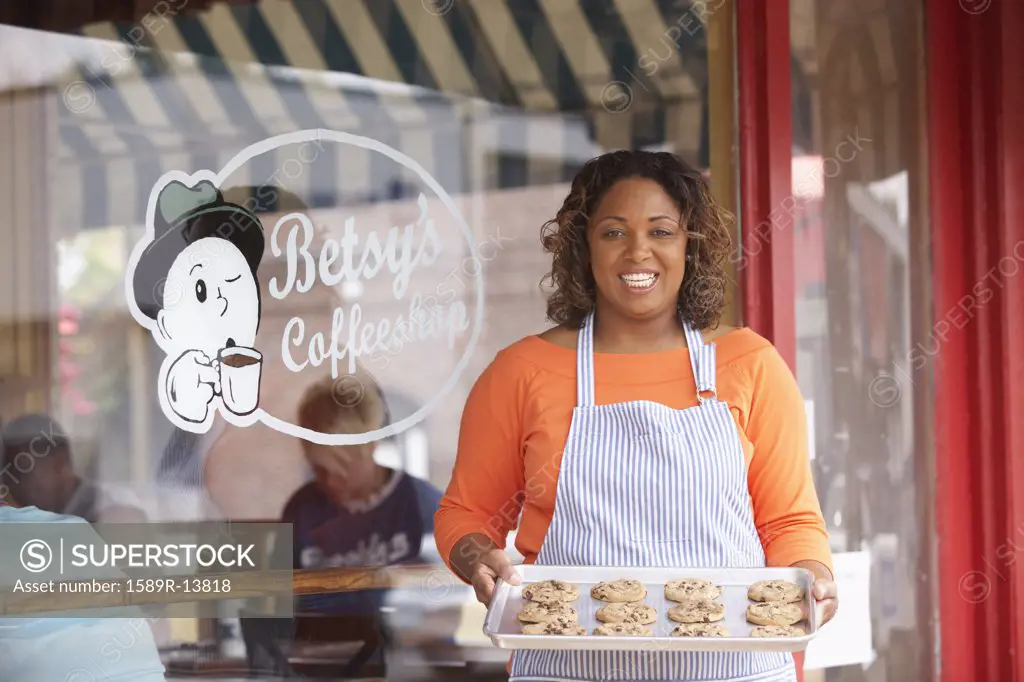 Portrait of woman with tray of cookies in front of coffee shop
