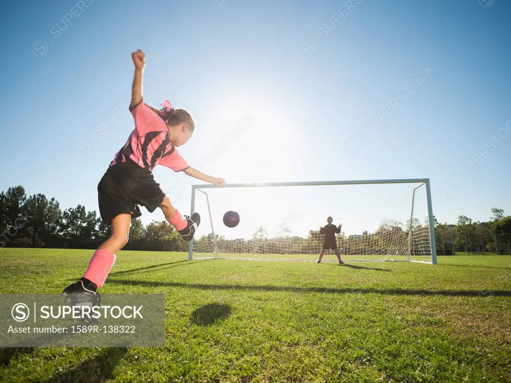 Girl soccer player kicking soccer ball at net