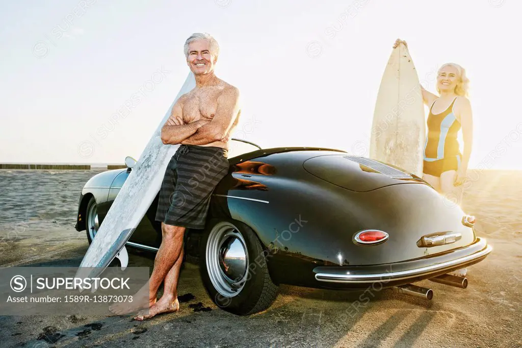 Older Caucasian couple on standing near convertible car with surfboards