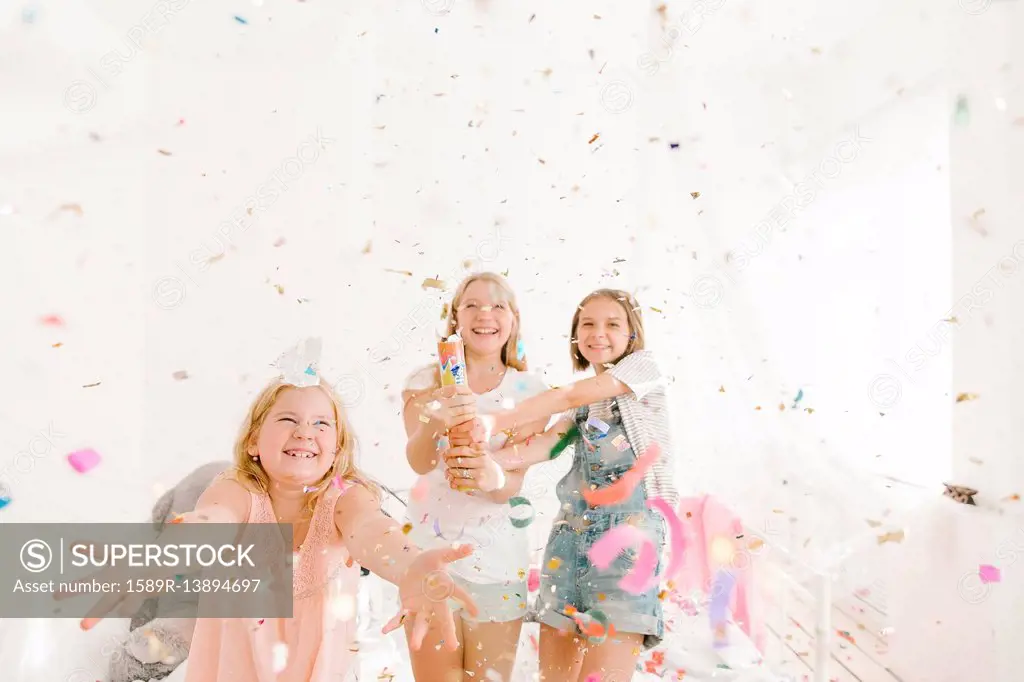 Smiling Middle Eastern girls throwing confetti in bedroom