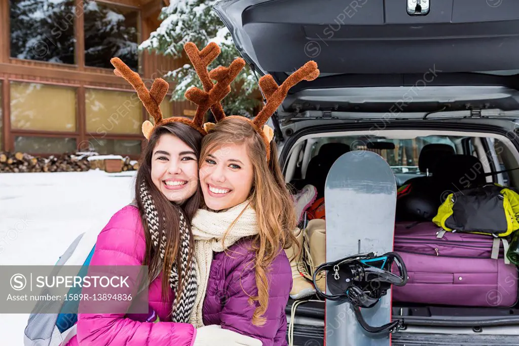 Women posing near car in winter wearing toy antlers