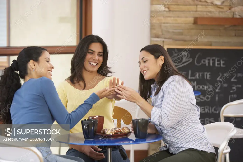 Three woman admiring engagement ring in cafe