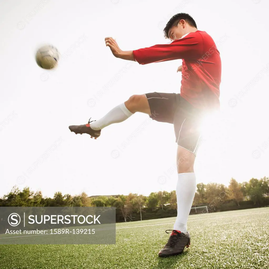 Asian soccer player kicking ball on soccer field