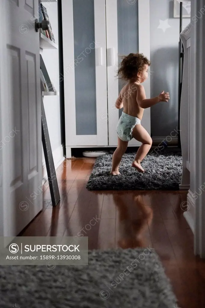 Caucasian boy wearing diaper running in corridor