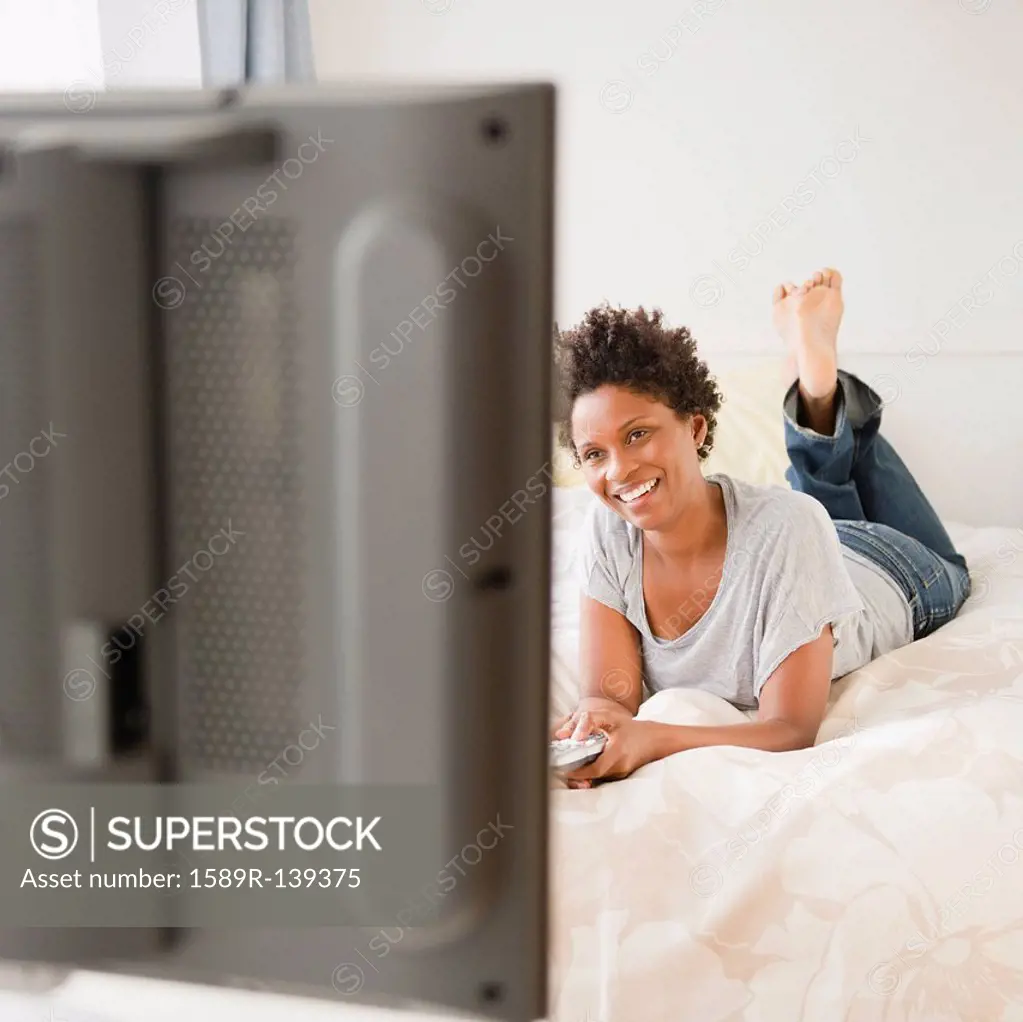 Black woman laying on bed watching television