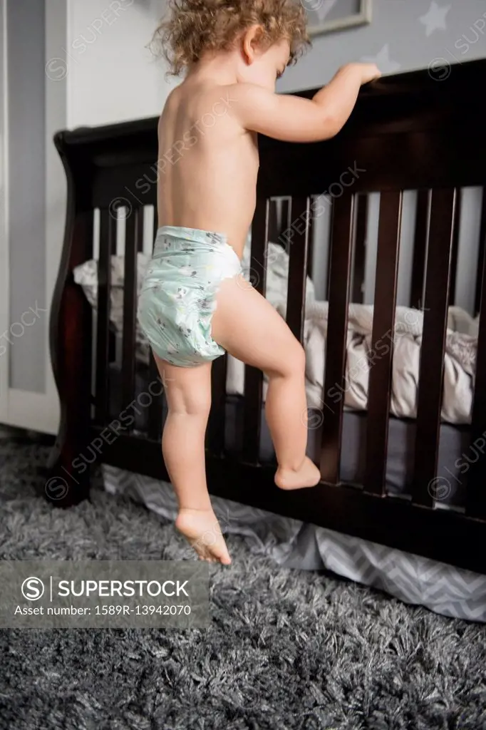 Caucasian boy wearing diaper climbing on bed frame