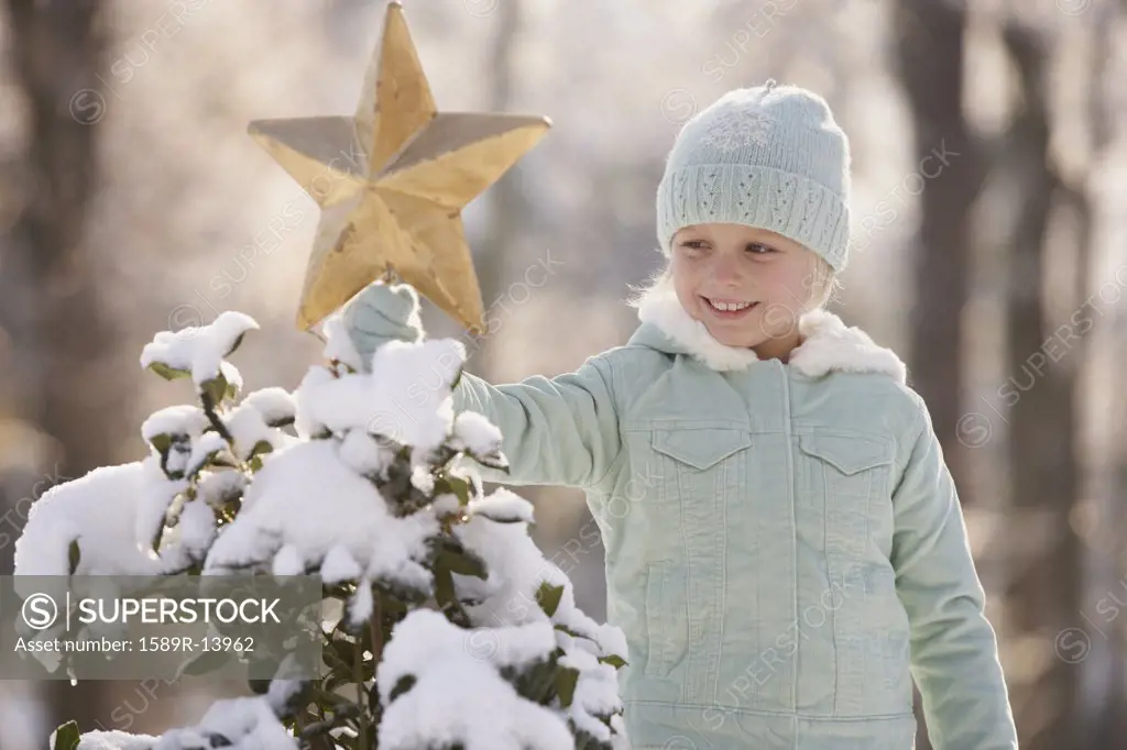 Young girl decorating a snowy Christmas tree with a star