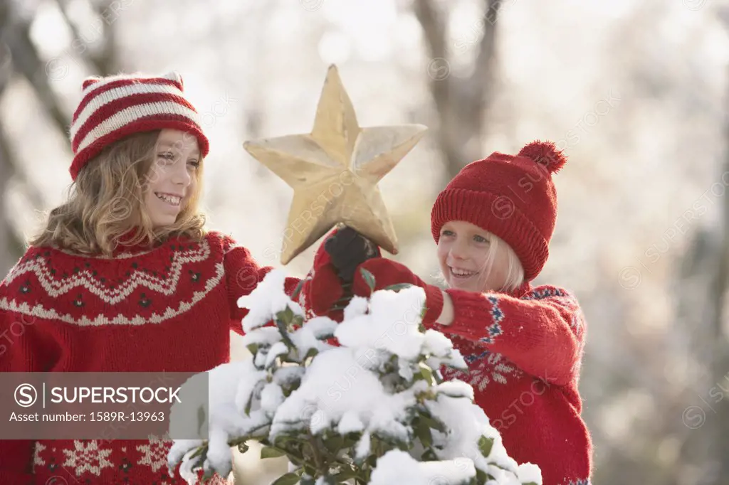 Young girls decorating a snowy Christmas tree with a star