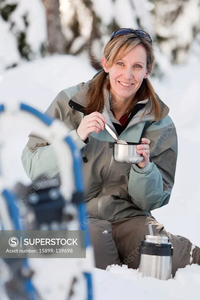 Caucasian woman with snowshoes eating in snow