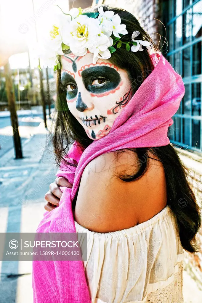 Mixed Race woman on sidewalk wearing scarf and skull face paint