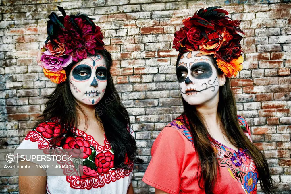 Women near brick wall wearing skull face paint