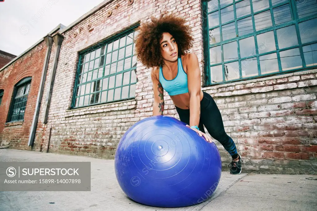 Hispanic woman balancing on fitness ball near brick wall