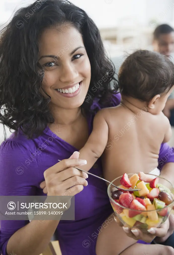 Mother holding baby and eating fruit salad