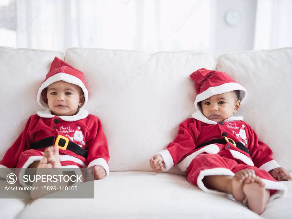 Twins on sofa dressed in Santa outfits