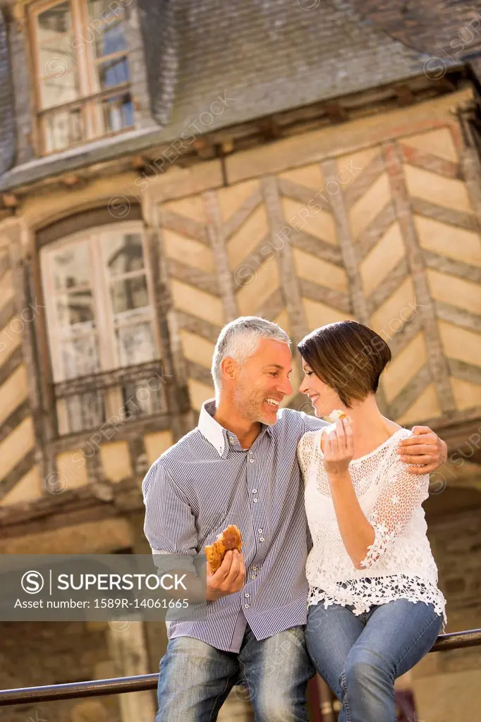 Caucasian couple eating bread on railing