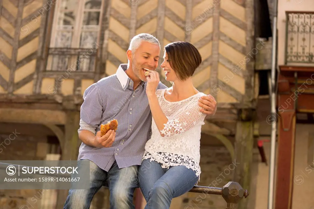 Caucasian couple eating bread on railing