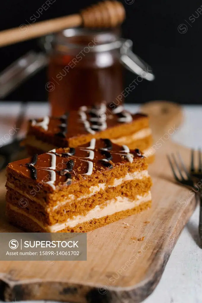 Slices of layer cake on cutting board with honey
