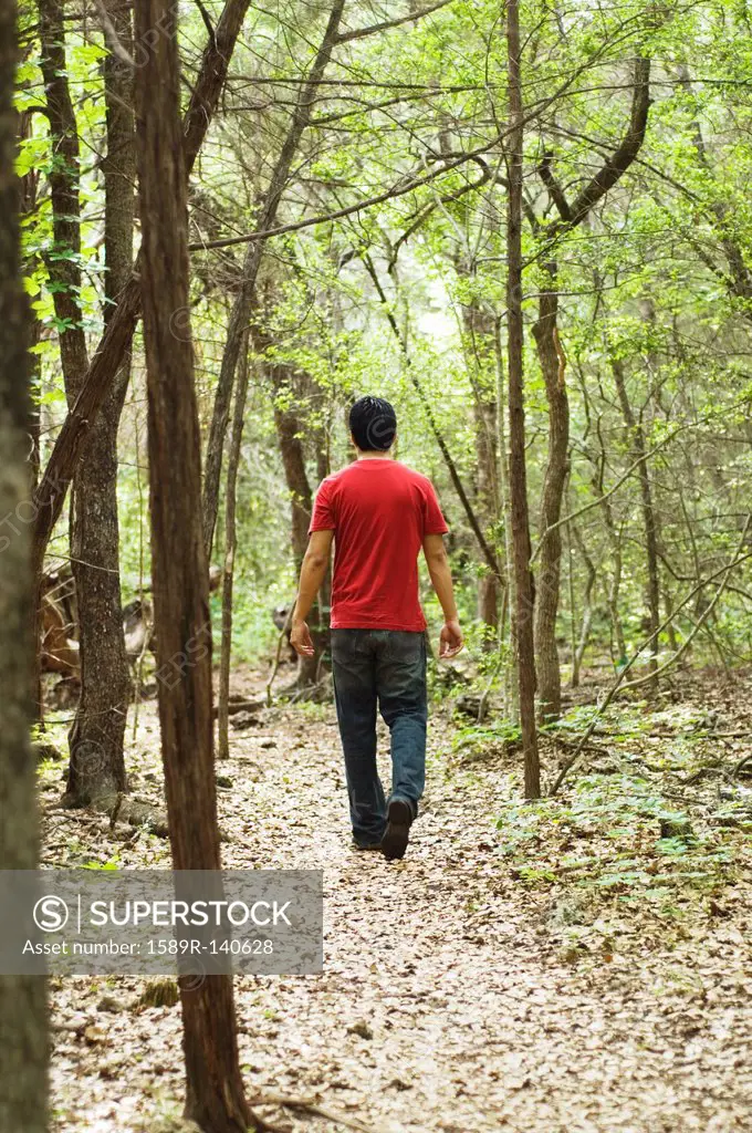 Hispanic man walking on path in woods