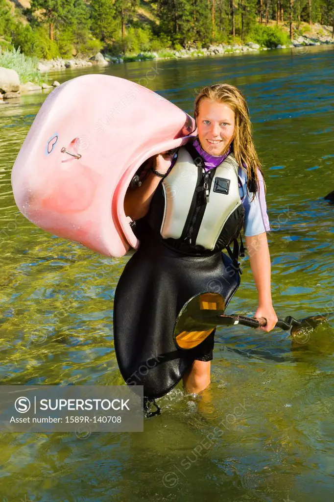 Caucasian teenager carrying kayak in river