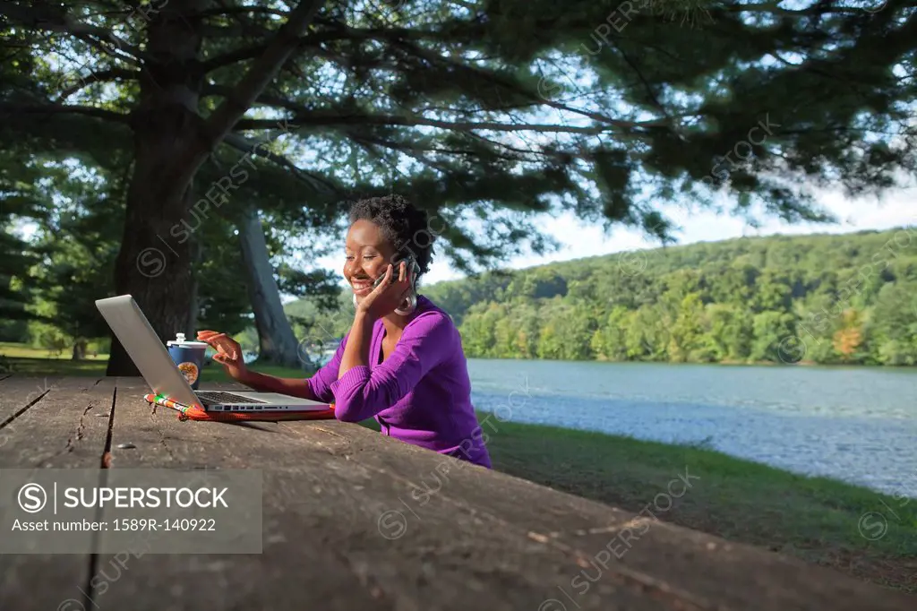 African American businesswoman sitting at picnic bench talking on cell phone