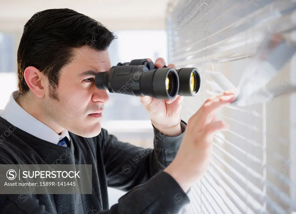 Hispanic businessman peering through window with binoculars