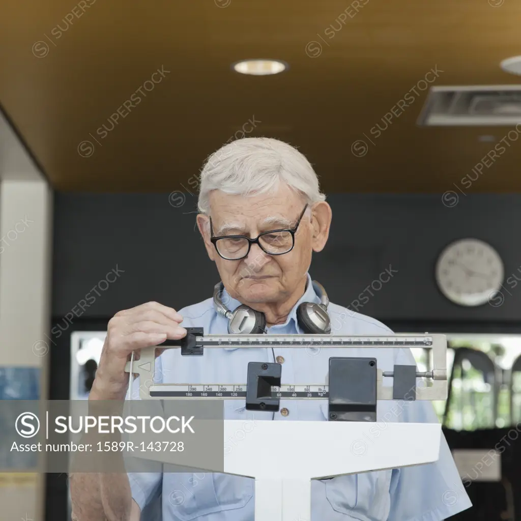 Senior man weighing himself in health club