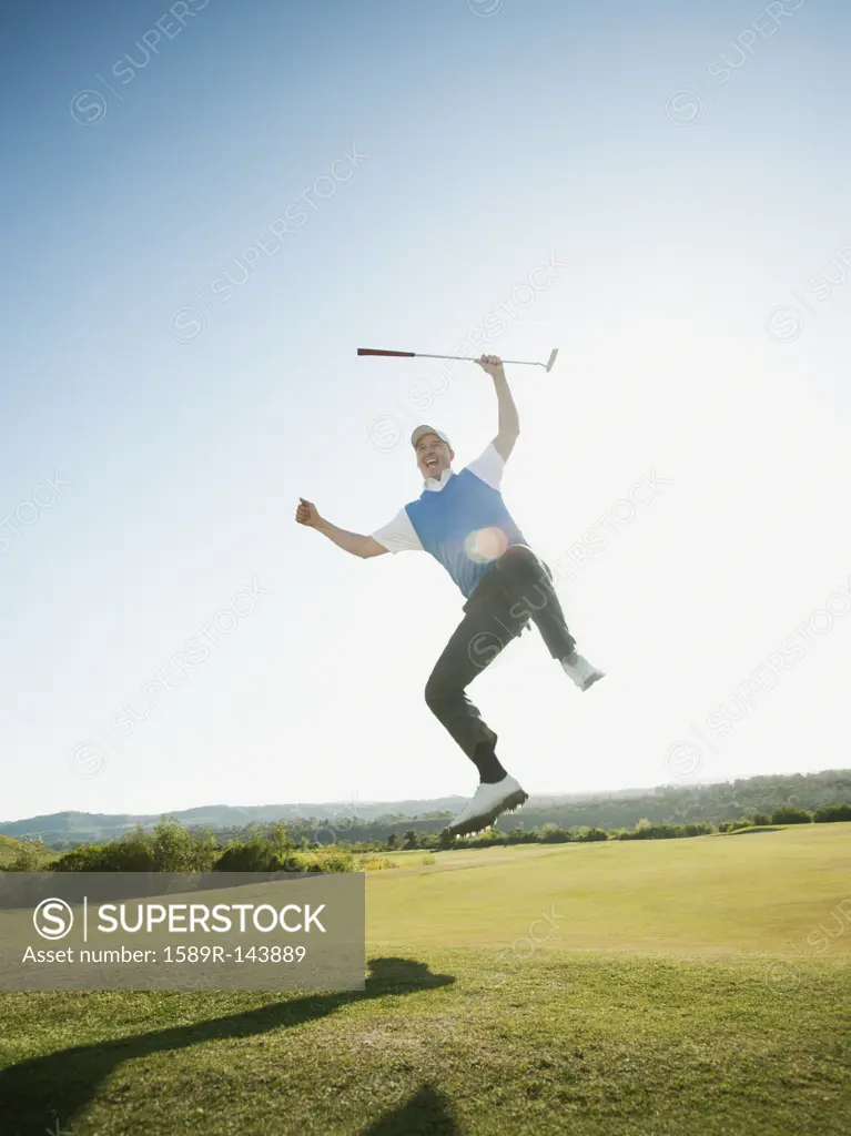 Excited Caucasian golfer jumping in mid_air on golf course