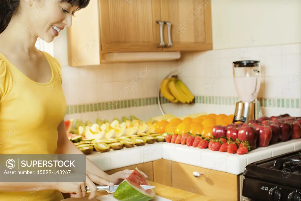 Mixed race woman cutting watermelon in kitchen
