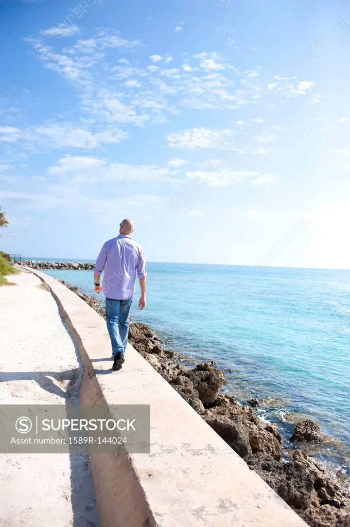 Hispanic man walking on wall near ocean
