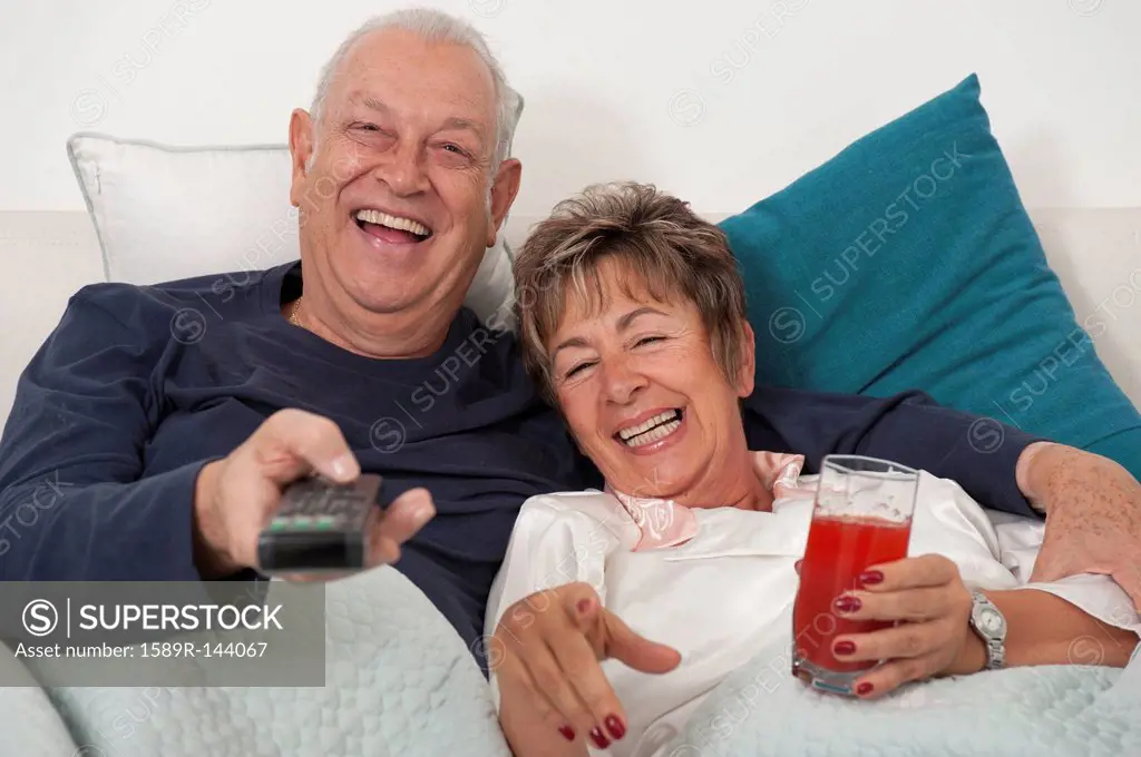 Senior Hispanic couple laying in bed watching television