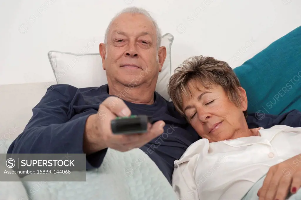 Senior Hispanic couple laying in bed watching television