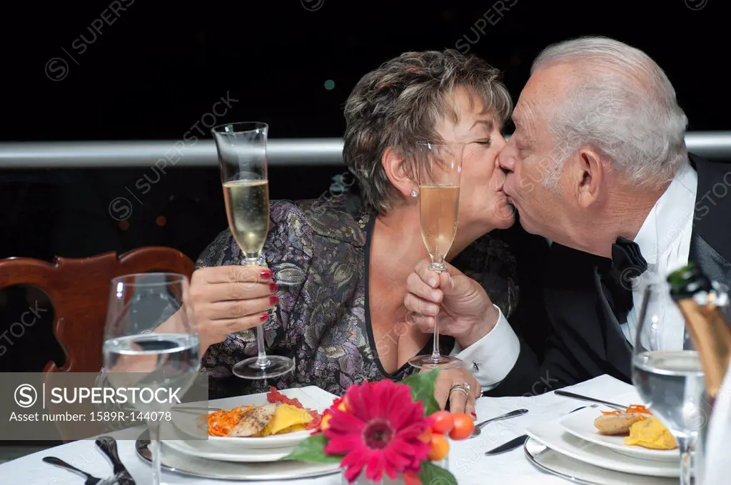 Kissing Hispanic couple toasting with Champagne in restaurant