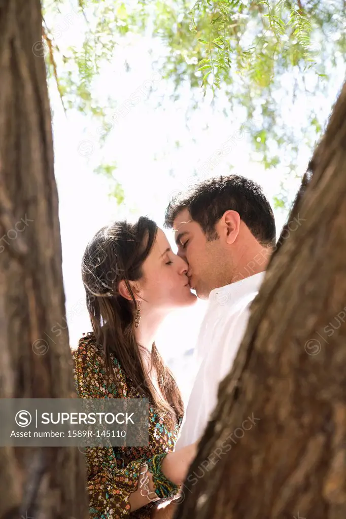 Hispanic couple kissing underneath tree