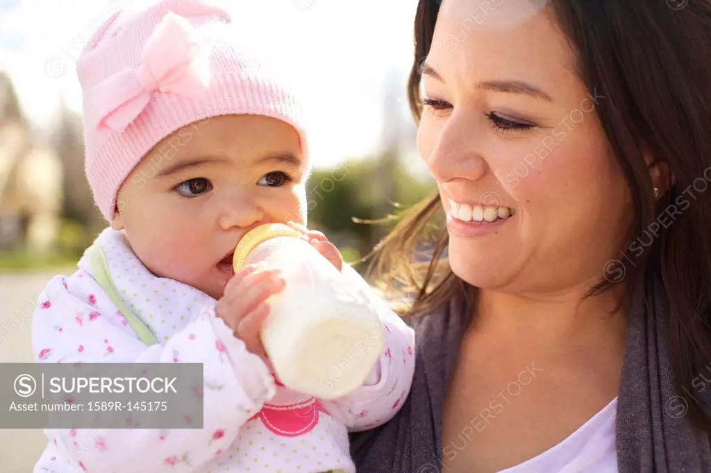 Mixed race mother watching baby girl drinking bottle